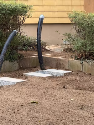 Vorbereitete Wärmepumpen-Fundamente mit Leitungswegen zwischen Gartenbeeten